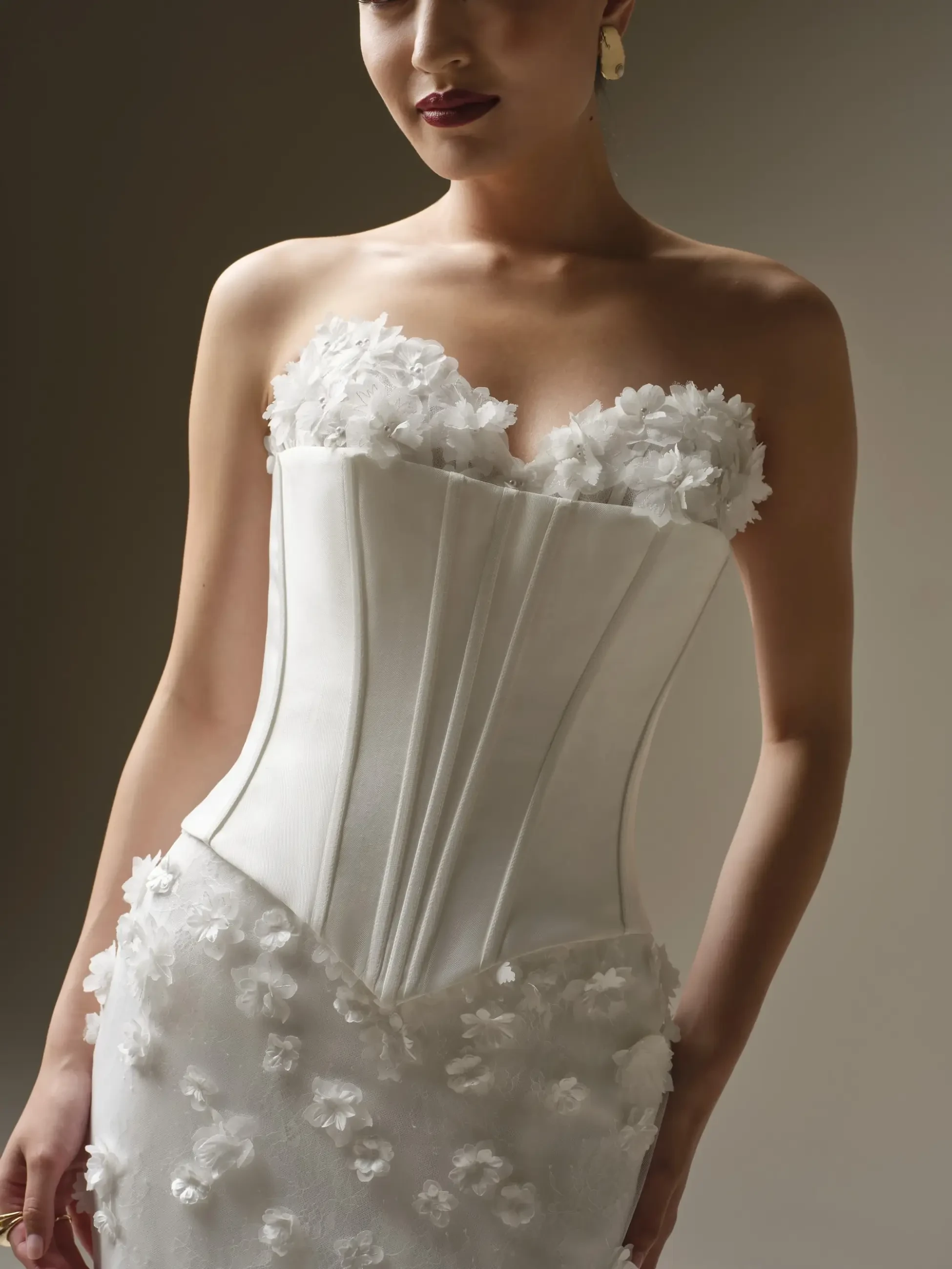 Woman in an elegant white dress with floral appliqu&eacute;s on the bodice and skirt. The setting is softly lit, conveying a sophisticated and graceful tone.